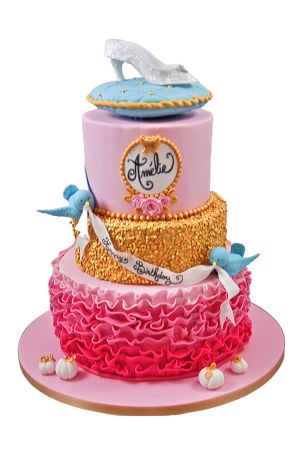 Luxe drie-laags verjaardagstaart met roze roesjes, gouden pailletten niveau, blauwe vogeltjes met een lint, mini pompoenen en een glazen muiltje op een kussen gemaakt door The French Cake Company