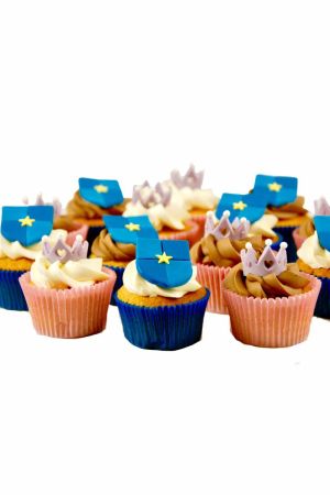 A collection of cupcakes with vanilla and chocolate frosting, decorated with 3D sugar crowns and blue shields featuring a yellow star.