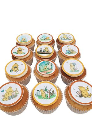 Een verzameling verjaardagscupcakes met eetbare ronde toppers met klassieke Winnie de Poeh en vriendjes illustraties.