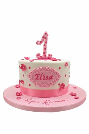 Pretty pink and white baby 1st birthday cake adorned with polka dots, sugar blossoms, and a polka-dot number 1 topper by The French Cake Company