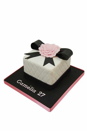 Gâteau d'anniversaire boîte cadeau carrée blanche matelassée avec nœud en fondant noir et fleur de camélia rose sculptée par The French Cake Company