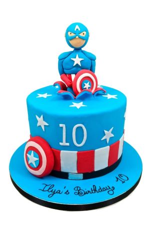 Bright blue round birthday cake featuring white stars, red and white stripes, fondant shield, and a 3D Captain America character bursting out from the top by The French Cake Company