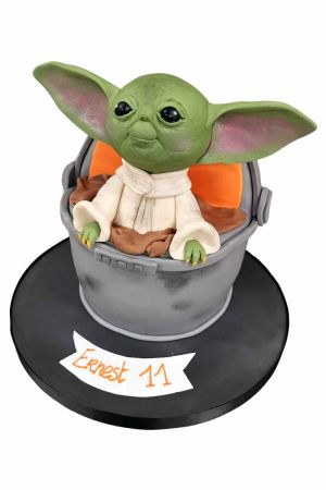 Un gâteau 3D sculpté représentant Grogu (Bébé Yoda) dans son landau flottant gris, posé sur un socle noir.