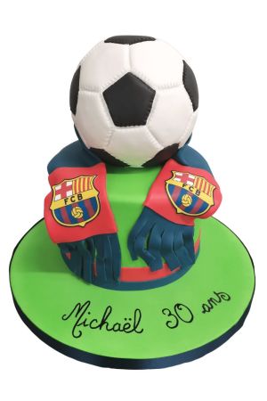 A circular football cake decorated with FC Barcelona's crest and colors, featuring blue and red stripes and an edible ball on top.