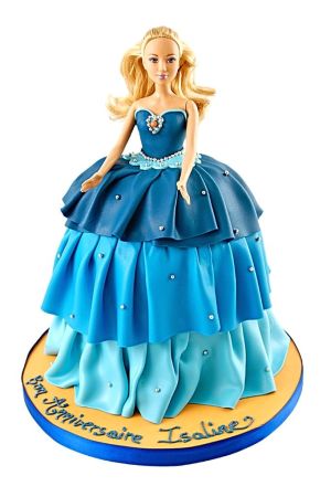 Blonde Barbie doll cake featuring a tiered ombre blue ruffled gown decorated with silver sugar pearls on a yellow round cake board by The French Cake Company