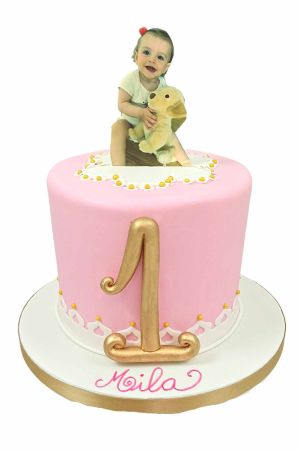 Exclusieve roze verjaardagstaart voor een eerste verjaardag afgewerkt met witte kant, gele suikerpareltjes, een gouden getal 1 en een eetbare foto van een baby bovenop, van The French Cake Company.