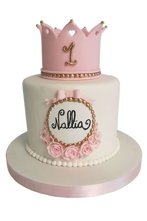 Luxe witte 1e verjaardagstaart gekroond met een roze prinsessenkroon, gouden parels en suikerrozen gemaakt door The French Cake Company