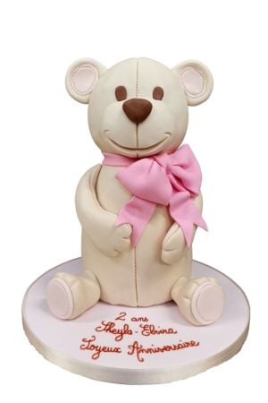 Un grand ours en peluche pastel est posé sur un gâteau magnifiquement décoré, idéal pour une fête de fille.