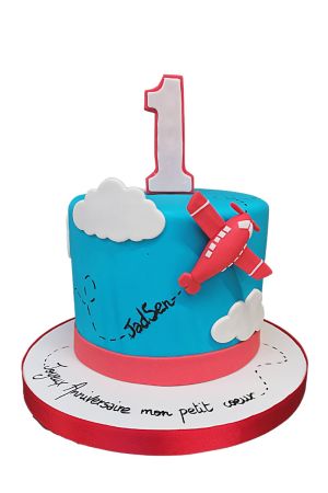 Un avion jouet rouge est posé sur un gâteau d'anniversaire glacé bleu, orné de petits nuages blancs, conçu pour la célébration du premier anniversaire d'un bébé.