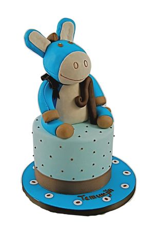 Lichtblauwe verjaardagstaart met bruine spikkels, gedecoreerd met een grote 3D handgemaakte blauw met beige Noukies Paco de ezel op een blauw plateau gemaakt door The French Cake Company