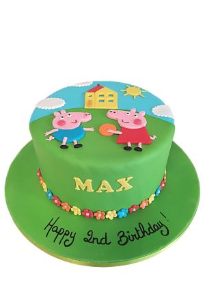 Gâteau d'anniversaire vert prairie bordé de petites fleurs multicolores, décoré de décors en pâte à sucre de Peppa Pig et George jouant au ballon devant leur maison jaune sous un ciel bleu ensoleillé réalisé par The French Cake Company