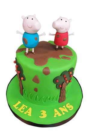Gâteau d'anniversaire vert herbe décoré de pommiers en sucre, d'éclats de boue et des figurines 3D de Peppa Pig et George sautant dans une grande flaque de boue marron réalisé par The French Cake Company