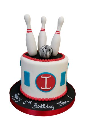 Gâteau d'anniversaire blanc sur le thème du bowling avec motifs géométriques bleus, perlages rouges, une boule marbrée et trois quilles blanches en sucre réalisé par The French Cake Company