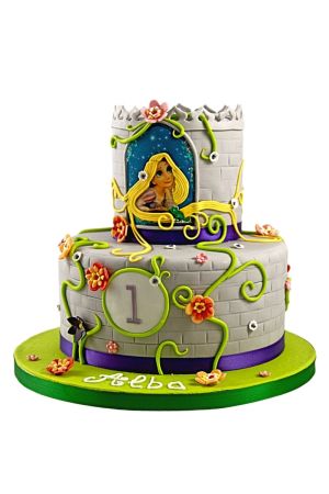Een verjaardagstaart met twee lagen gedecoreerd als een grijze stenen kasteeltoren met groene lianen, gekleurde bloemetjes en een eetbare afbeelding van Rapunzel met lange gouden haren die naar beneden vallen.