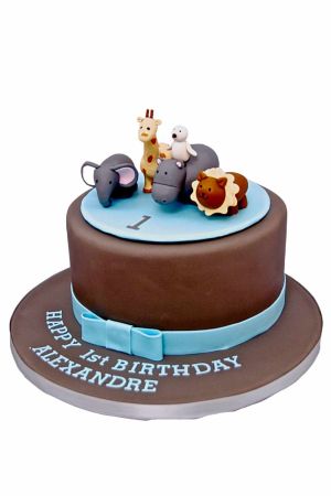 Exclusieve bruine verjaardagstaart voor jongens in Jacadi jungle stijl met een lichtblauwe strik, een schijf met het getal 1 en ambachtelijke 3D dierfiguren van een olifant, giraf, nijlpaard en leeuw, van The French Cake Company.
