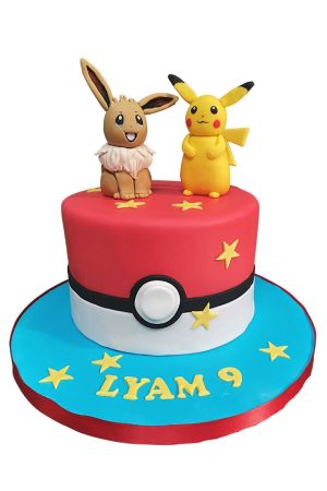 Un gâteau d'anniversaire rond en pâte à sucre reprenant le design d'une Pokéball rouge et blanche, surmonté de modelages comestibles d'Évoli et de Pikachu, avec un prénom et l'âge sur le socle bleu.