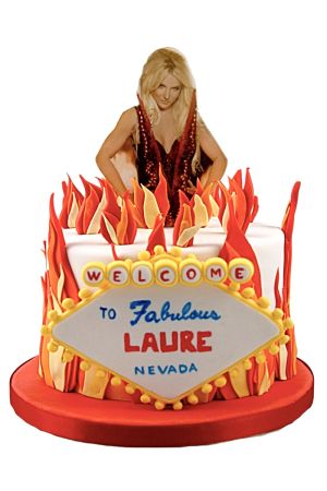 Un gâteau d'anniversaire rond en pâte à sucre blanche, entouré de flammes rouges et orange sculptées, décoré d'un panneau de bienvenue style Las Vegas au nom de Laure, surmonté d'une photo de Britney Spears.