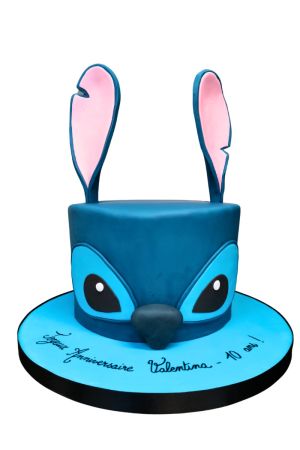 A dark blue fondant birthday cake sculpted to look like the character Stitch's face, featuring tall blue and pink 3D ears.