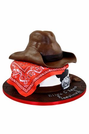 3D sheriff cowboy hat birthday cake with a red paisley bandana and silver badge on a wooden effect board
