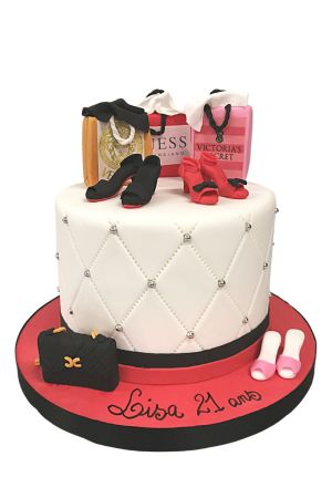 Un gâteau d'anniversaire blanc matelassé décoré de miniatures comestibles de sacs de shopping de luxe et de chaussures à talons.
