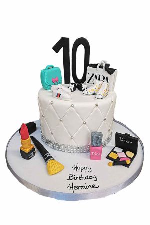 Een witte gecapitonneerde fondant taart met zilveren parels, versierd met eetbare lippenstift, kwasten, een Zara tasje en het cijfer 10.