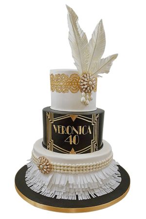 Pièce montée d'anniversaire chic à trois étages thème Gatsby style art déco noir, blanc et or avec franges blanches, perles comestibles, dentelle dorée et grandes plumes blanches, créée par The French Cake Company.