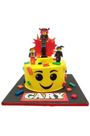 Custom The Lego Movie birthday cake shaped like a yellow minifigure face, topped with handcrafted 3D sugar characters Emmet, Wyldstyle, and Lord Business, by The French Cake Company.
