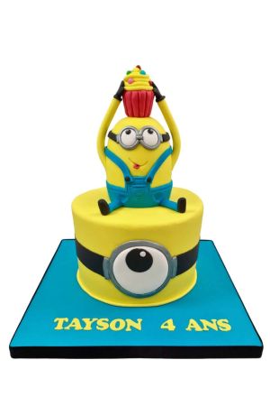Exclusieve gele Minion verjaardagstaart met een groot duikbril-oog op de basis en een handgemaakt 3D Minion figuurtje met een cupcake bovenop, van The French Cake Company.