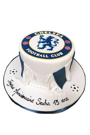 n overhead shot of a rectangular Chelsea football cake, decorated with blue and white icing to represent the club's colors. The Chelsea FC crest is prominently displayed on top, and a white border adorns the edges. The cake is centered on a white surface.