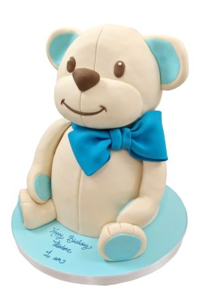 Une vue rapprochée d'un gâteau en forme d'ours en peluche décoré de glaçage blancs et d'accents bleu , conçu pour la célébration d'un anniversaire de garçon.