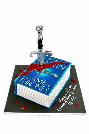 Gâteau d'anniversaire personnalisé 3D en forme de livre Game of Thrones bleu, transpercé par une épée en sucre avec effets rouges, créé par The French Cake Company.