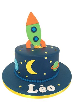 Dark blue birthday cake decorated with a yellow moon, stars, planets, and a green 3D rocket ship topper