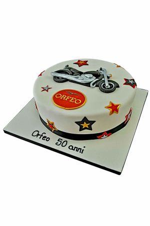 Un gâteau d'anniversaire blanc décoré d'étoiles rouges et dorées, d'un badge Moto Guzzi et d'une figurine de moto noire en sucre au sommet.