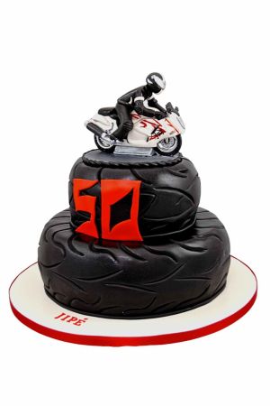 Pièce montée personnalisée d'anniversaire à deux étages en forme de pneus de moto noirs, surmontée d'une figurine de moto de course japonaise blanche, créée par The French Cake Company.