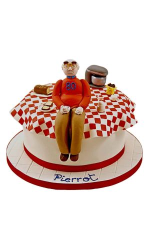 Gâteau d'anniversaire personnalisé représentant une table de petit-déjeuner avec nappe à carreaux rouges et blancs, modelage d'un homme avec son café, du pain et une cafetière, créé par The French Cake Company.