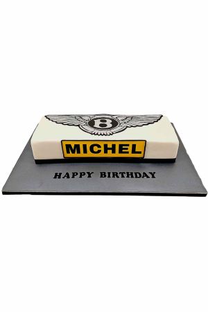 Gâteau d'anniversaire rectangulaire blanc chic avec logo ailé Bentley et plaque d'immatriculation jaune, présenté sur plateau gris, créé par The French Cake Company.