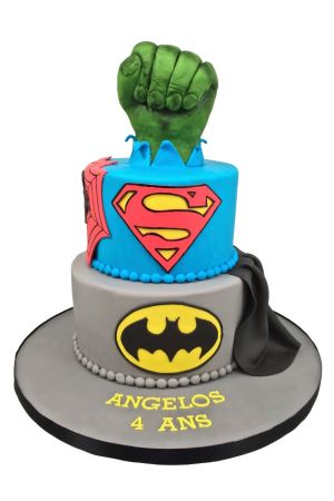 Een verjaardagstaart met twee lagen in blauw en grijs, versierd met het Superman- en Batman-logo en een grote groene Hulk-vuist bovenop.