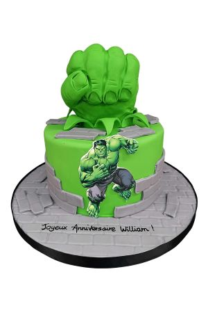 A green Hulk-themed birthday cake with a large edible green fist on top and grey fondant bricks around the base.