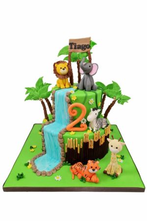 Exclusieve dubbellagige jungle verjaardagstaart met een waterval van fondant, palmbomen, een oranje getal 2 en ambachtelijke 3D dierfiguren van een leeuw, olifant, zebra, giraf en tijger, van The French Cake Company.