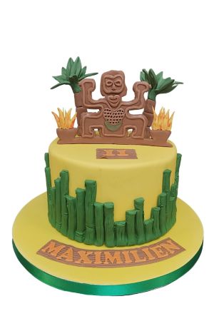 Un gâteau d'anniversaire jaune orné de bambous en sucre verts et d'un totem tribal avec des palmiers au sommet.