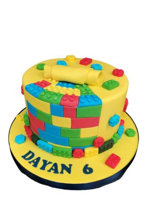 Custom round Lego theme birthday cake covered in yellow fondant revealing a colorful wall of sugar building blocks and loose colorful Lego bricks, by The French Cake Company.