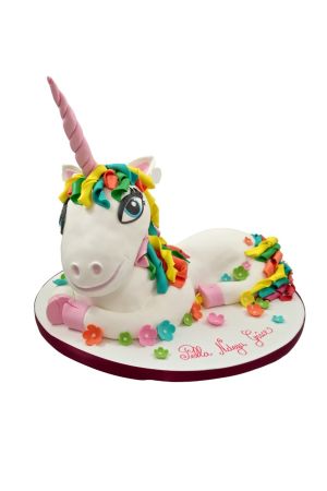 Custom 3D sculpted lying unicorn birthday cake featuring a pink twisted horn, colorful sugar mane and tail, and small fondant flowers scattered around the base, handcrafted by The French Cake Company.
