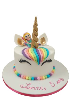Custom white unicorn birthday cake featuring a shimmering golden horn, rainbow sugar mane, pearl border, and a 3D fairy figurine, handcrafted by The French Cake Company.