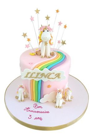 Custom round pink birthday cake decorated with a colorful fondant rainbow, sugar clouds, shooting star toppers, and multiple handcrafted 3D baby unicorn figurines, by The French Cake Company.