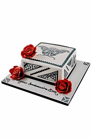 Un gâteau d'anniversaire carré blanc décoré de motifs graphiques noirs de style tatouage et de trois roses rouges sculptées en sucre.