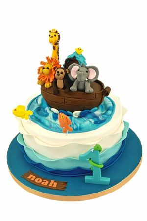 Exclusieve Ark van Noach verjaardagstaart gedecoreerd met blauwe oceaangolven, springende visjes, het getal 1 en een houten boot gevuld met ambachtelijke 3D dieren zoals een leeuw, aap, olifant en giraf, van The French Cake Company.