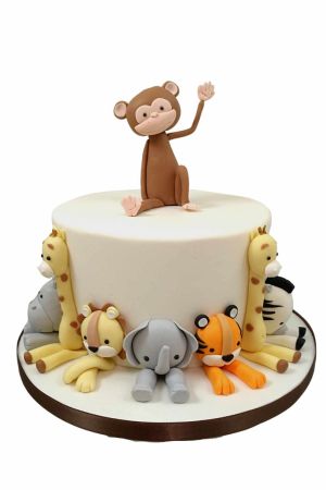 Exclusieve witte verjaardagstaart in jungle thema met een zwaaiend 3D aapje bovenop en ambachtelijke suikerfiguren van een leeuw, tijger, olifant, giraf, zebra en nijlpaard rondom de basis, van The French Cake Company.