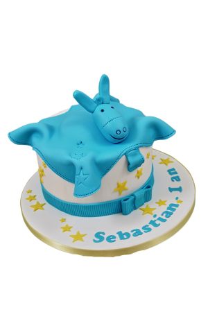 Gâteau du 1er anniversaire blanc à étoiles jaunes, ruban bleu canard et couverture doudou l'âne Paco de Noukie's modelée en pâte à sucre avec sa tête 3D réalisé par The French Cake Company