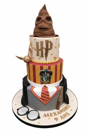 Une pièce montée d'anniversaire à trois étages en pâte à sucre représentant un uniforme de Poudlard en bas, des rayures bordeaux et jaunes au milieu avec le blason Gryffondor, et un sommet blanc surmonté d'un grand Choixpeau magique en 3D.