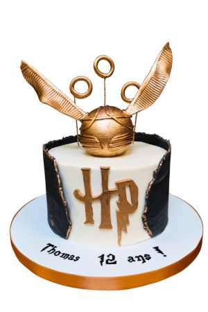 Un gâteau d'anniversaire rond en pâte à sucre blanche décoré du logo doré HP, enveloppé d'un effet de cape noire déchirée aux contours dorés, surmonté d'un grand Vif d'Or métallique sculpté et de trois anneaux de Quidditch.